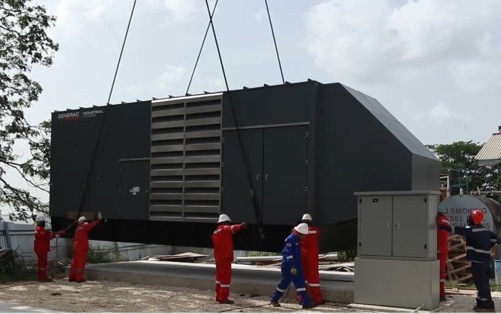 Technicians installing industrial power generator via crane